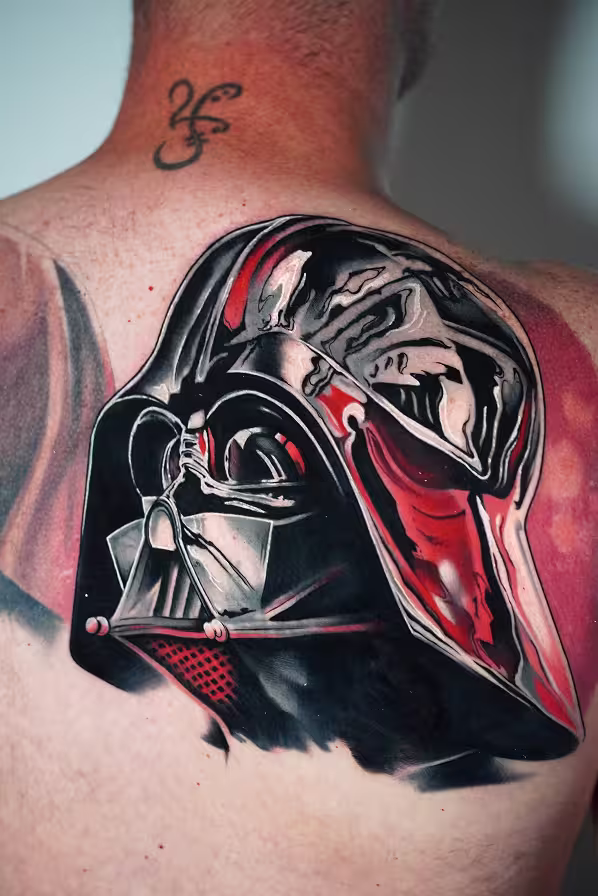 Large back tattoo depicting Darth Vader's helmet cracking open to reveal a monstrous screaming face underneath, in dramatic black and red tones with a realistic style