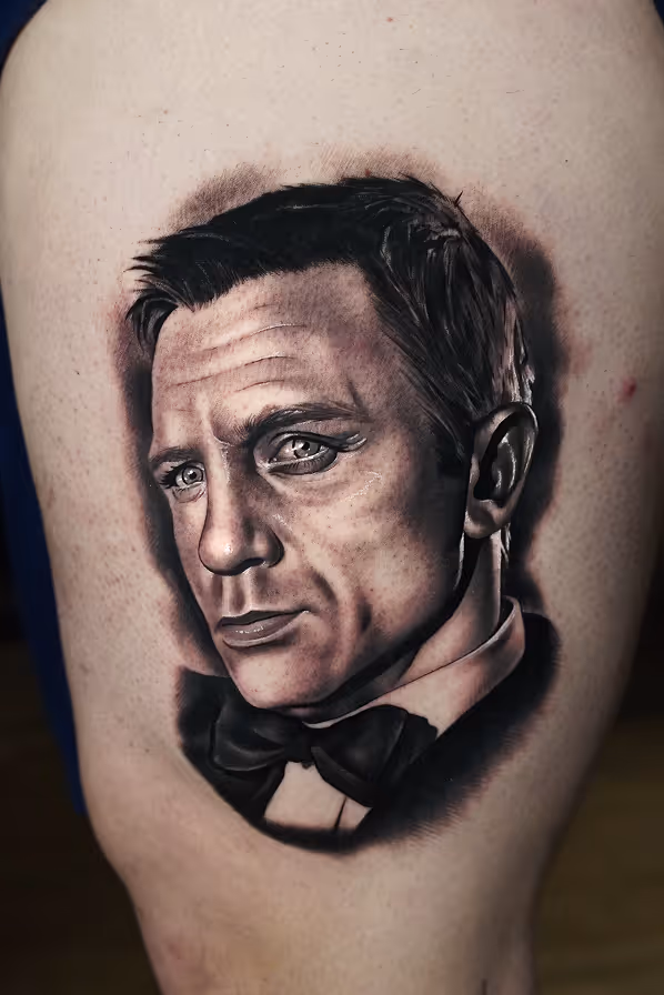 Black and grey realistic tattoo of a agent 007 James Bond wearing a bow tie, showing detailed facial features and short hair.