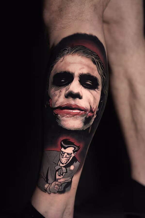 Tattoo of two Joker depictions on a leg, one realistic face with white makeup and red lips, and one cartoonish character holding a gun.