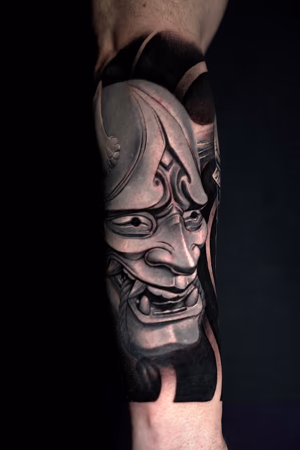 Black and gray tattoo of a detailed Japanese Oni mask on a person's forearm.